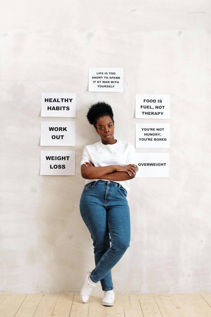 A woman standing against a wall with signs promoting healthy lifestyle habits and messages.